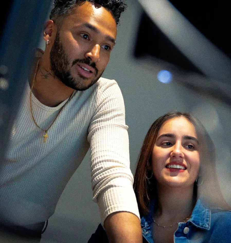 A man and woman working together in an office, engaged with a laptop screen in front of them.