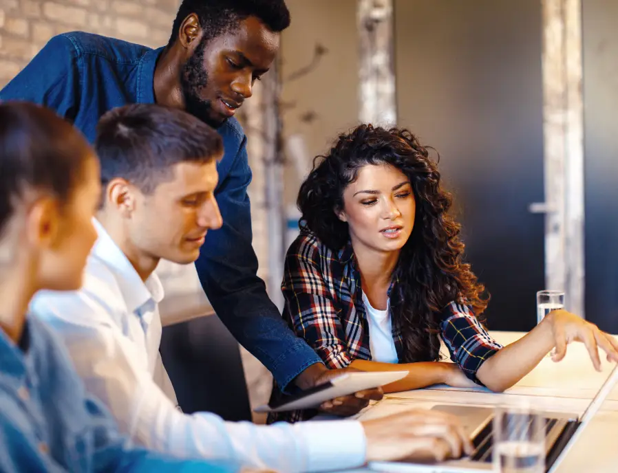 Several individuals engaged in teamwork, gathered around a laptop, discussing and contributing to a shared task.