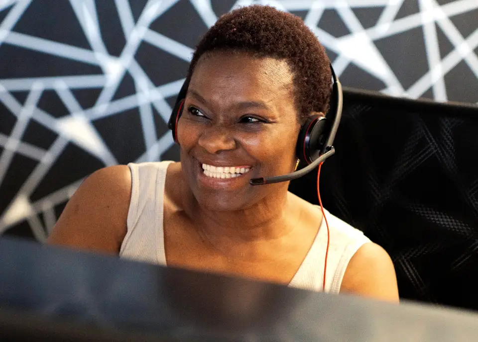 A woman in a headset smiles as she works at her computer, reflecting a cheerful and professional atmosphere.
