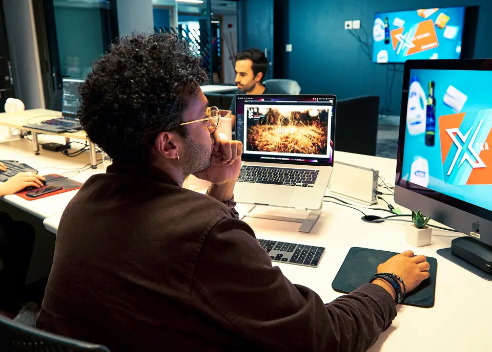 Two colleagues sitting at separate desks, each working on their own computers in a shared office space.